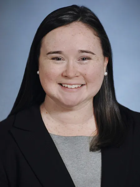 Woman smiling with dark hair, dark jacket, and light colored shirt.